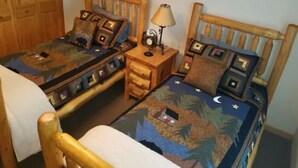 Una habitación con dos camas de madera, cada una con un diseño de colcha diferente. Hay cuadros enmarcados en la pared y una mesita de noche de madera con una lámpara entre las camas.