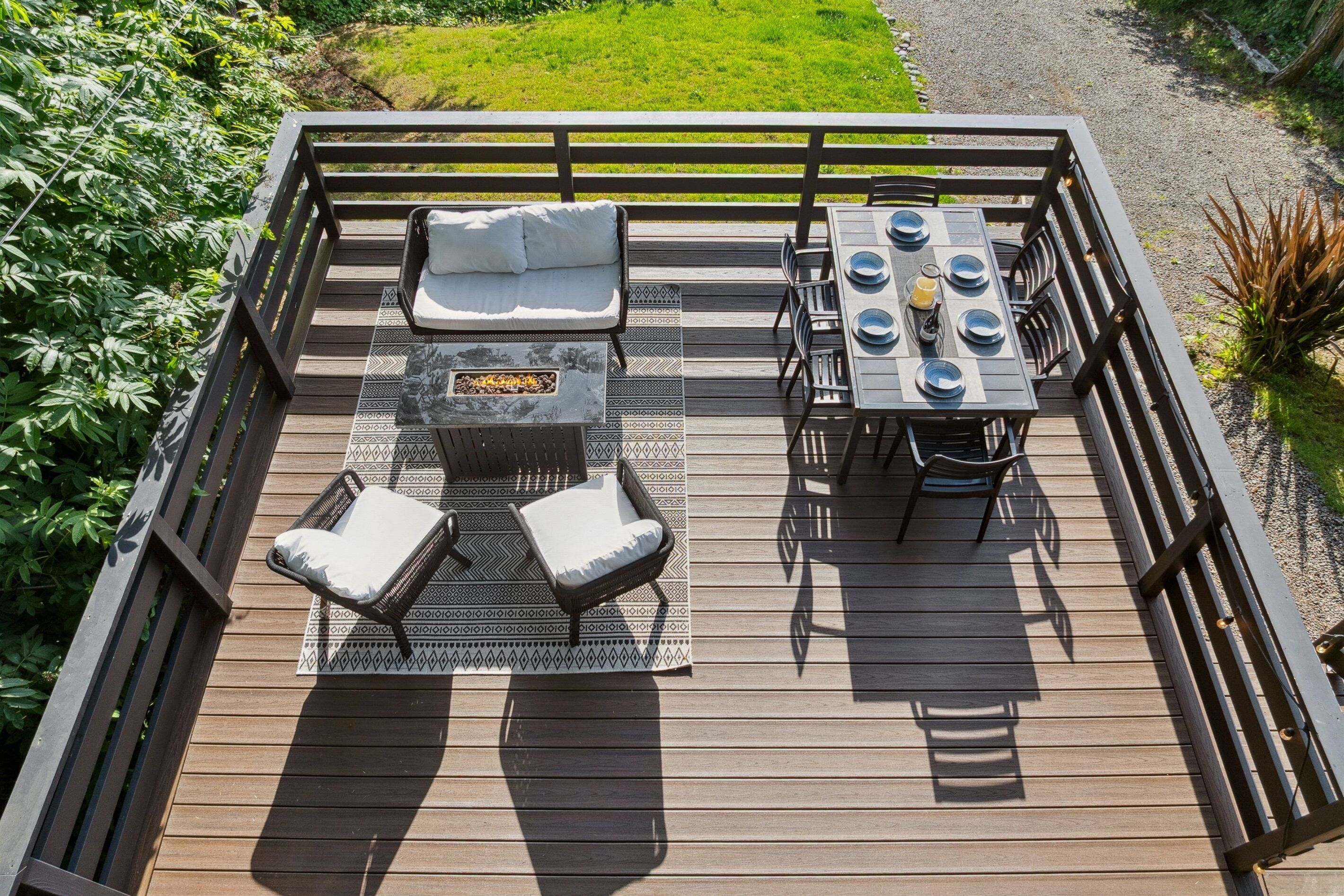 Una terraza de madera con una zona de estar integrada, un hogar y una mesa dispuesta para comer.