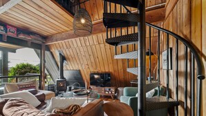 A cozy cabin interior with a wooden interior, a fireplace, a TV, and a spiral staircase.