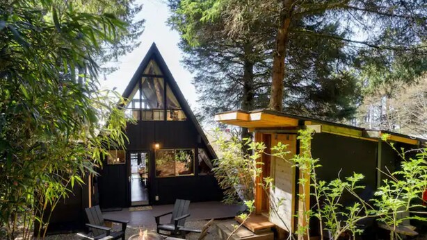 A cabin with a triangular roof, a deck with outdoor seating, and a small attached structure.