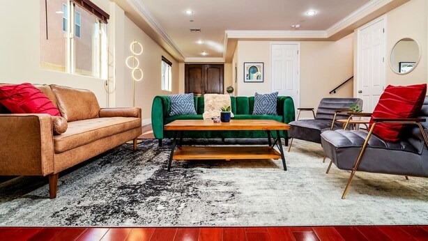 A living room with a brown leather sofa, a green velvet sofa, a wooden coffee table, and a grey armchair.