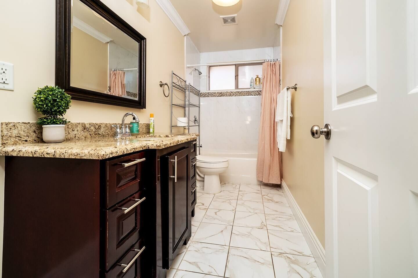 A bathroom with a marble floor, a sink with a granite countertop, a mirror above the sink, a toilet, and a shower area with a curtain.