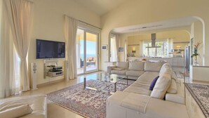 Een ruime woonkamer met een grote bank, een flatscreen-televisie aan de muur en een balkon met uitzicht.