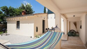 A covered outdoor area with a hammock, a barbecue grill, and a small building with a tiled roof.