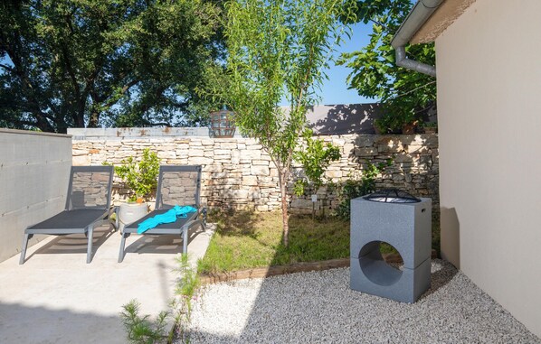 A patio area with a stone wall, a metal grill, and two lounge chairs.
