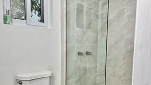 Un bany amb vàter, una cabina de dutxa de vidre i una finestra sobre el vàter.