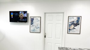 Habitació amb una porta blanca, un televisor penjat que mostra un programa i dos quadres abstractes emmarcades.