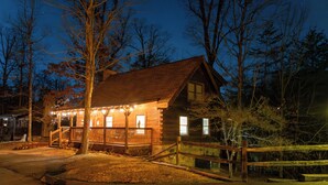 A log cabin with a porch, surrounded by trees and a wooden fence.