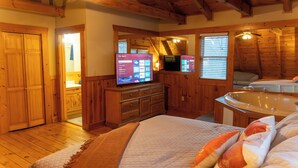 A wooden-paneled bedroom with a large bed, a TV, and a hot tub.