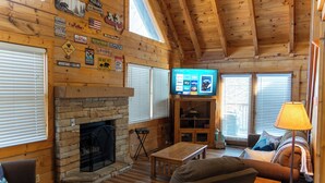 A log cabin interior with a stone fireplace, wooden walls, and a television mounted on the wall.