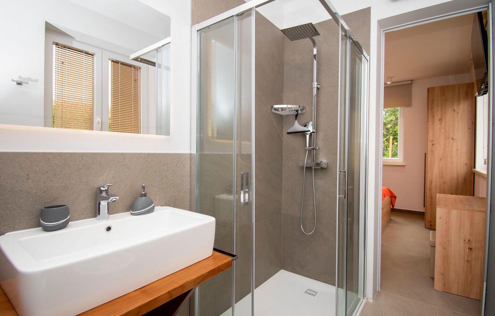Ein modernes Badezimmer mit einer gläsernen Duschkabine, einem weißen Waschbecken und einem Holzregal.