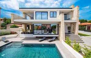 Une maison moderne à deux étages, dotée d’une piscine, d’un espace salon extérieur et offrant une vue sur le quartier environnant.