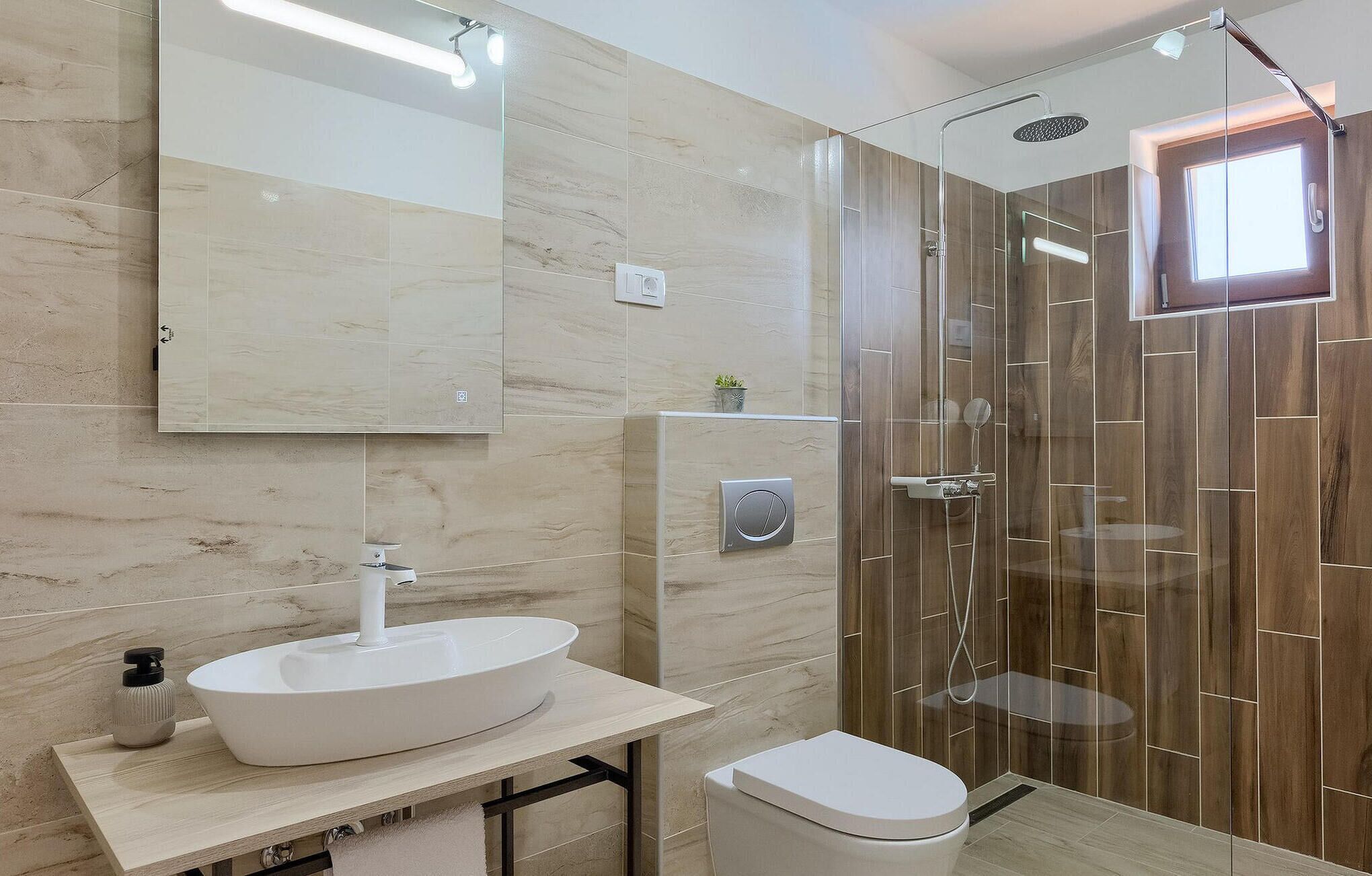 Une salle de bain moderne dotée d’un grand miroir, d’un lavabo sur colonne, de toilettes et d’une douche à l’italienne.