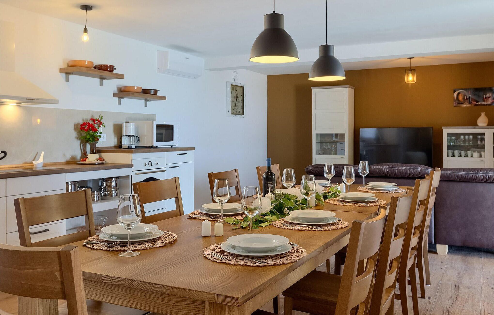 A modern kitchen with white cabinets, a microwave, and a coffee maker. There is a dining area with a wooden table set for six, surrounded by chairs.