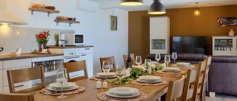 A modern kitchen with white cabinets, a microwave, and a coffee maker. There is a dining area with a wooden table set for six, surrounded by chairs.
