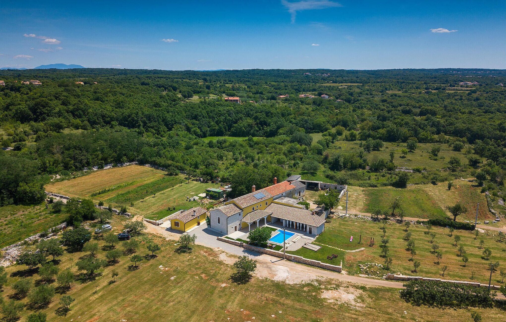 An aerial view of a property with a large house featuring a swimming pool, surrounded by lush greenery and fields.