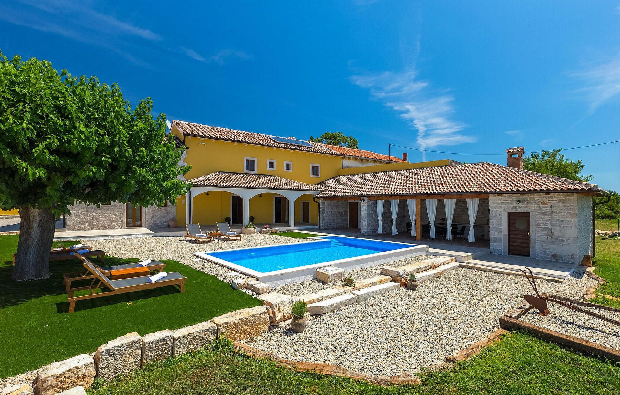 Eine Villa mit Swimmingpool, Sitzgelegenheiten im Freien und einem Garten.