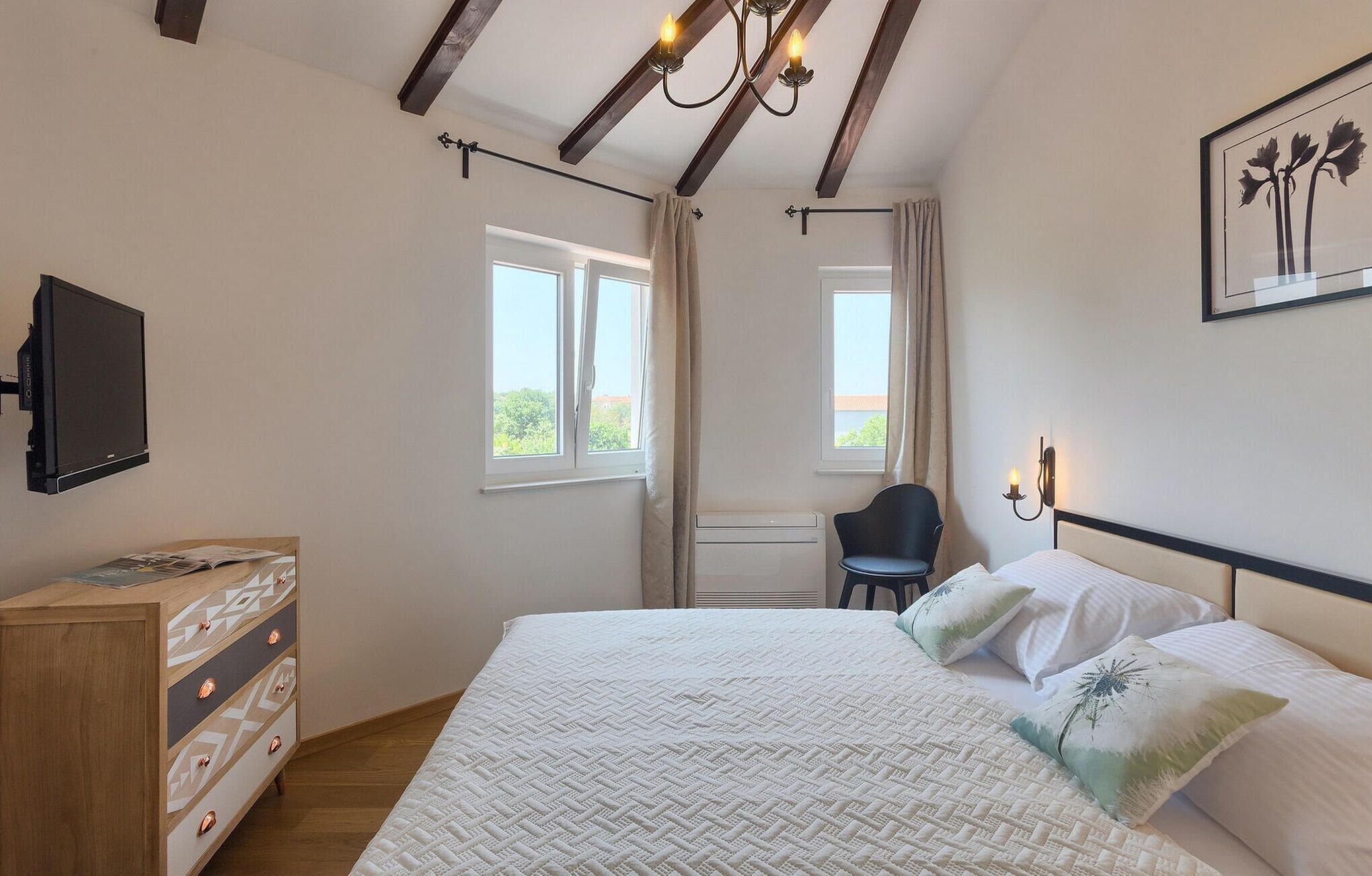 A bedroom with a bed, a chair, a desk, a TV, and a window.