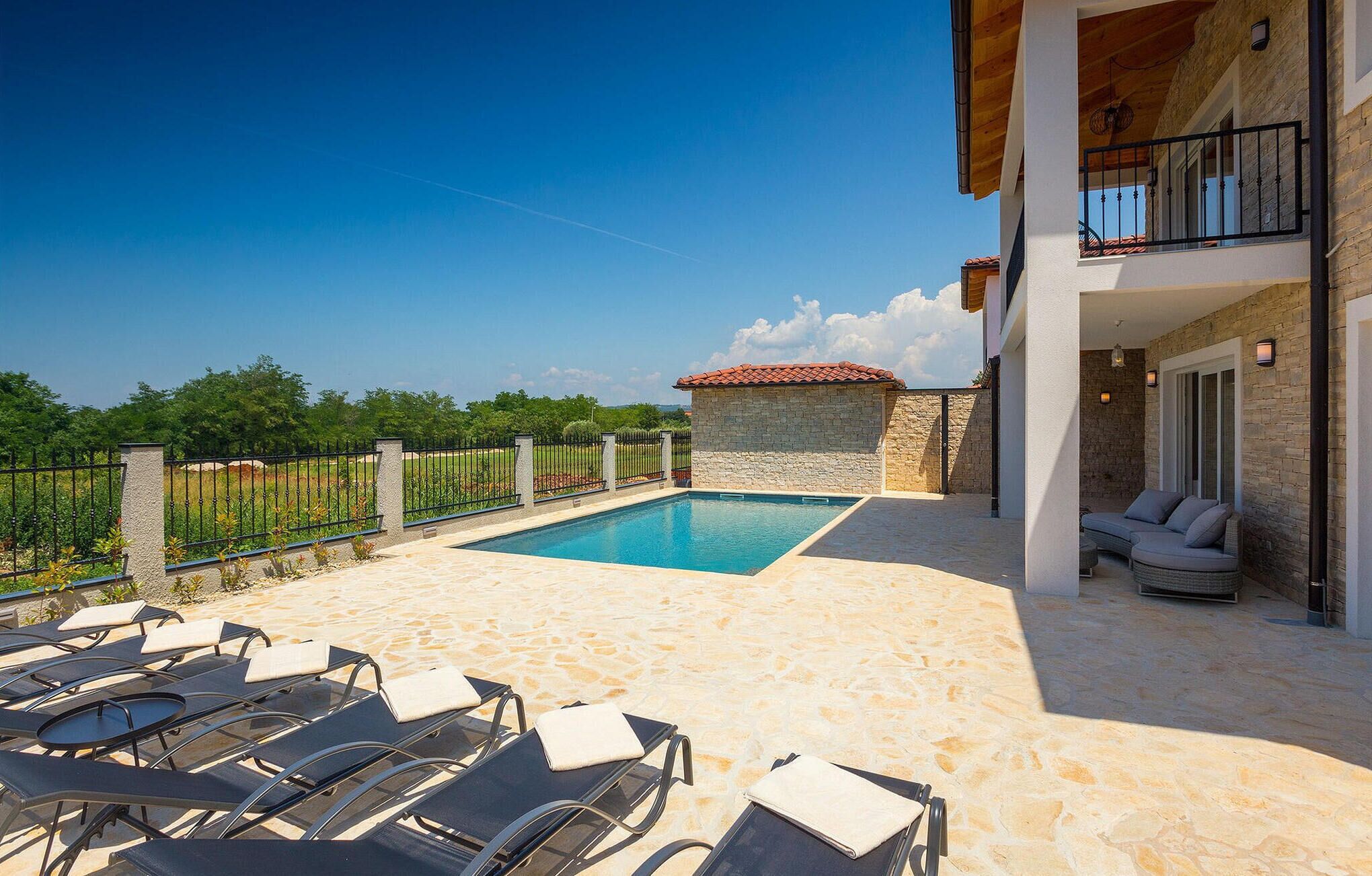A poolside area with lounge chairs, a stone wall, and a view of the countryside.