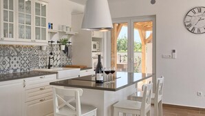 Une cuisine moderne avec des meubles blancs, un îlot central doté de tabourets de bar, une bouteille de vin et des verres.