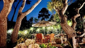 An outdoor seating area with a table and chairs under a canopy, surrounded by trees and plants. - Gorgeous 3-bdrm home, walk to town and beach (Carmel-by-the-Sea)