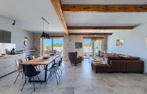 A spacious living area with a wooden ceiling, a stone wall, a large window, and a brown leather sofa. - Pet friendly home in Marcana (Marcana)
