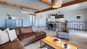 Een moderne woonkamer met een bruine leren bank, een houten salontafel en een eethoek met een grijze stoel en een bar.