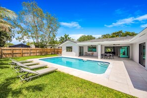 A backyard with a swimming pool, a wooden fence, and a patio with outdoor furniture.