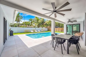 A modern outdoor patio with a pool, ceiling fans, and a dining area with chairs.
