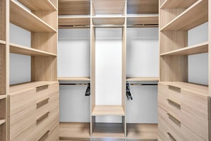 A walk-in closet with wooden shelving and drawers, featuring a central hanging rod and a mirrored closet door.
