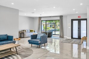 A modern lobby with a sofa, armchairs, a wooden bench, and a patterned rug.