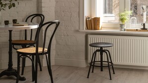A room with a white brick wall, a large window with a view of the outside, a round table with chairs, and a radiator below the window. - Lwowska Apartment (Warsaw)