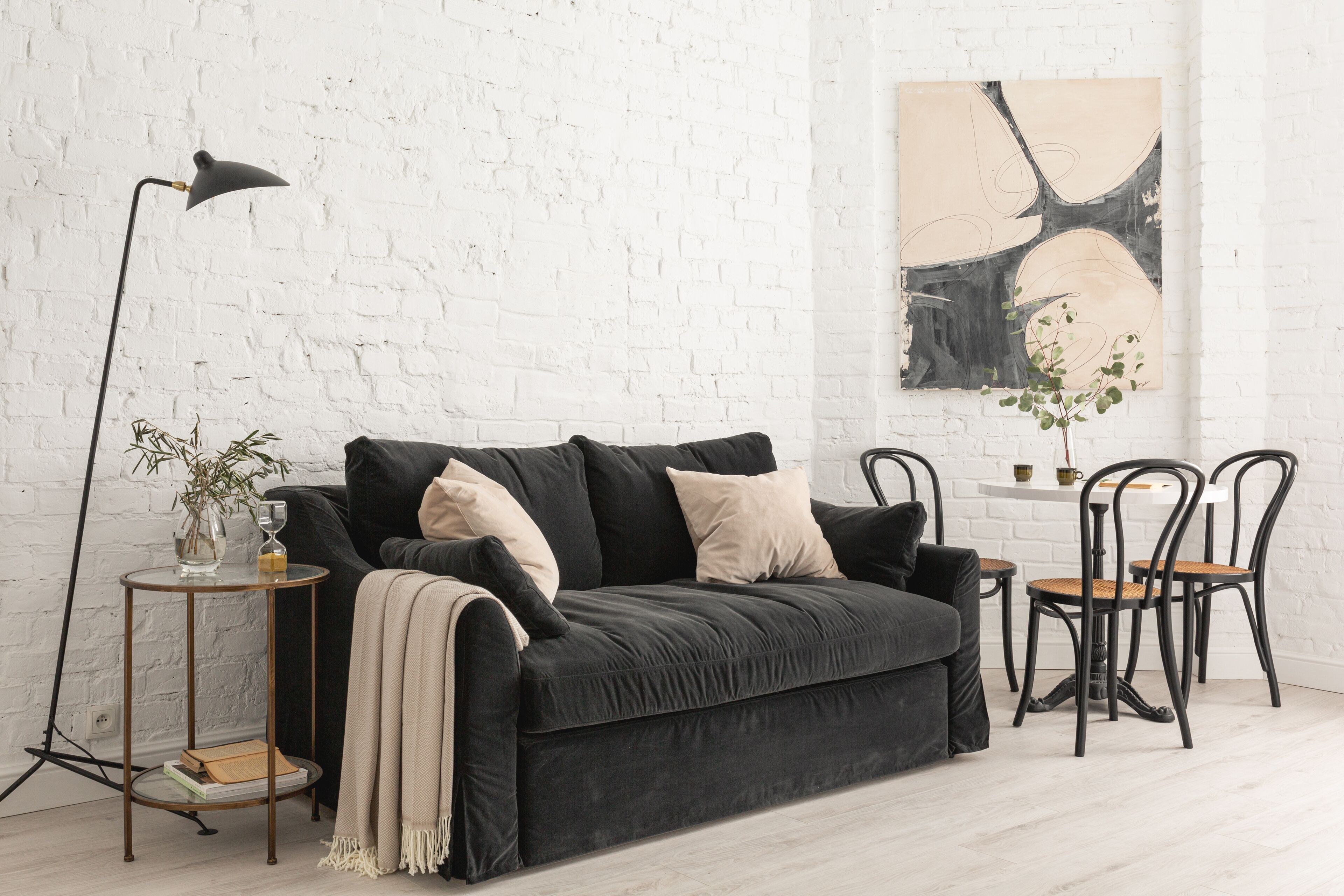 A modern living room with a dark grey sofa, a small side table with a lamp, and a minimalist painting on the wall.