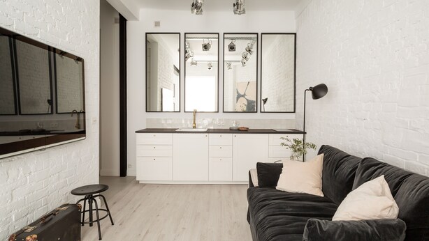 A modern kitchen with white cabinets, a black countertop, and a large mirror above the sink. - Lwowska Apartment (Warsaw)