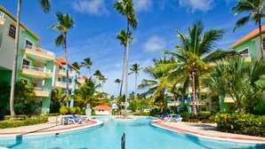 Ein Poolbereich eines Resorts mit Palmen, Liegestühlen und mehrstöckigen Gebäuden mit Balkonen.