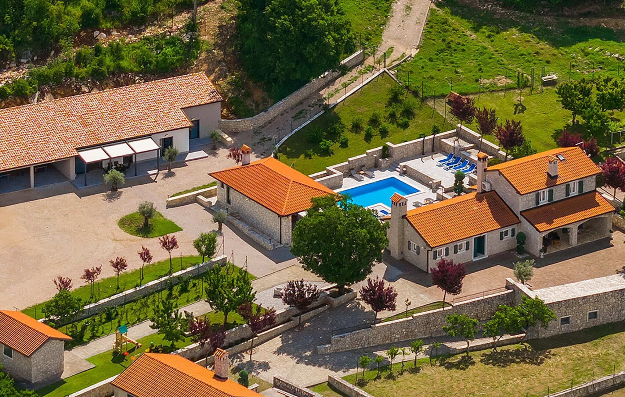 Vue aérienne d’un complexe hôtelier doté d’une piscine, de plusieurs bâtiments aux toits recouverts de tuiles et de jardins aménagés.
