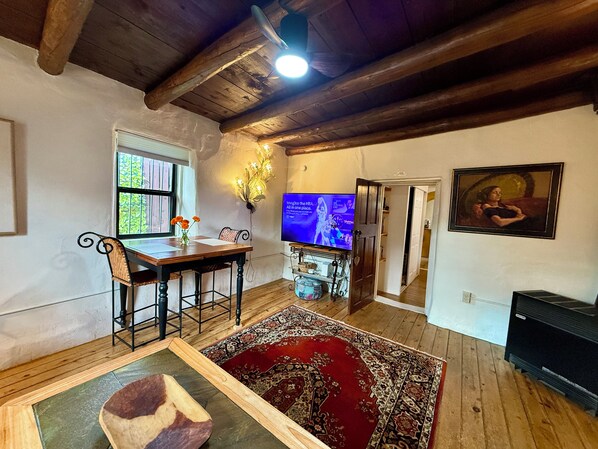 A living room with a wooden ceiling, a TV, a dining table, and a red patterned rug.
