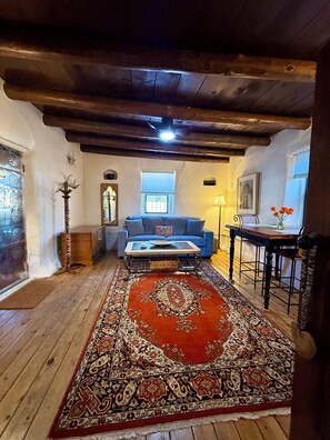A cozy living room with a blue sofa, a wooden coffee table, a patterned rug, and a dining table with chairs.