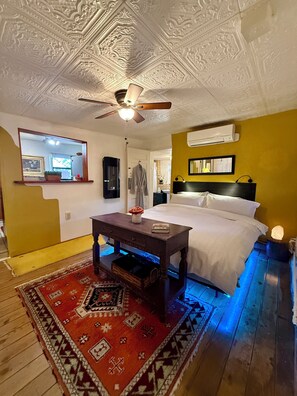 A bedroom with a bed, a ceiling fan, a nightstand, a mirror, and a wall-mounted air conditioner.