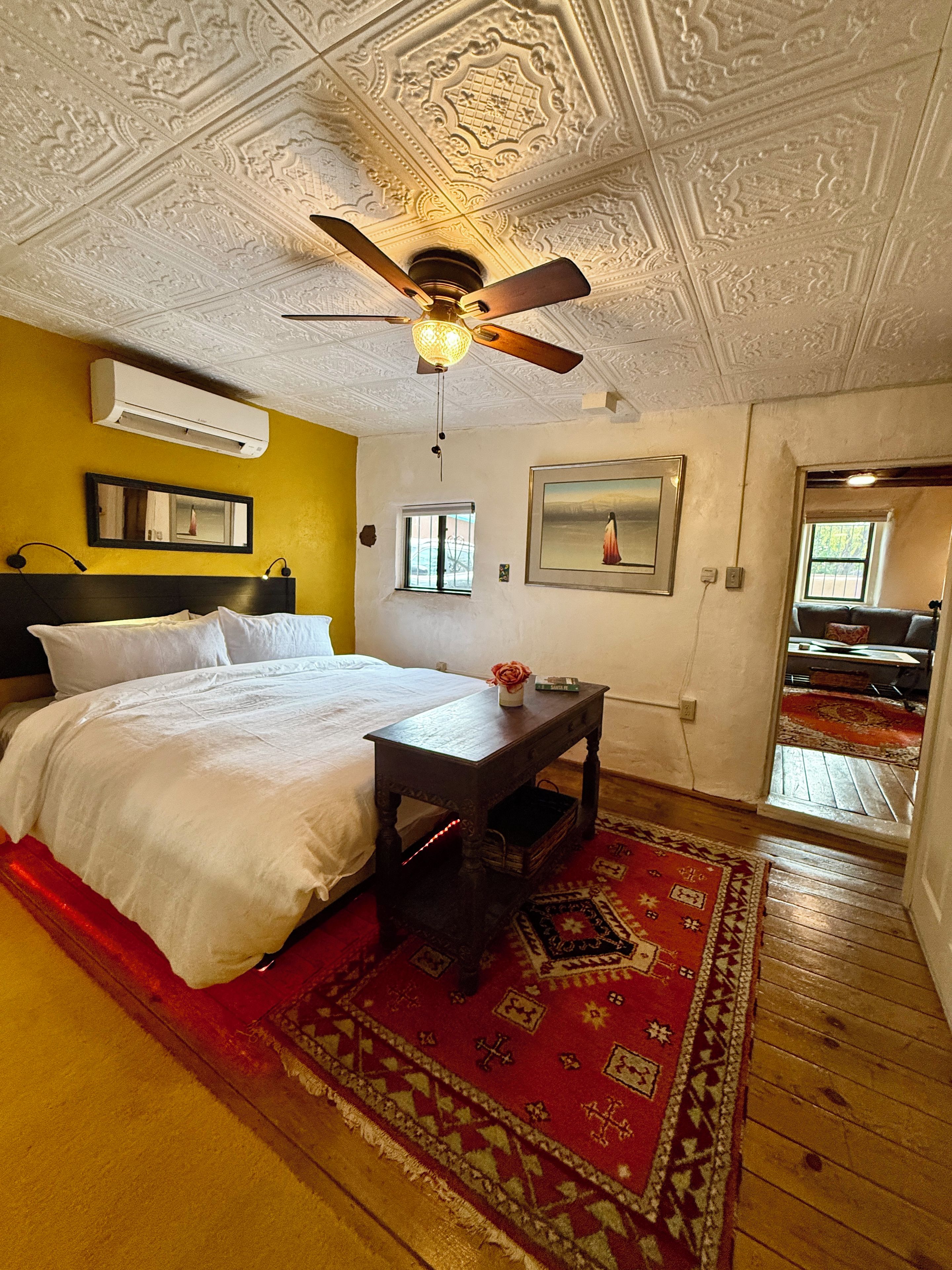 A bedroom with a bed, a ceiling fan, a nightstand, a red rug, and a window.