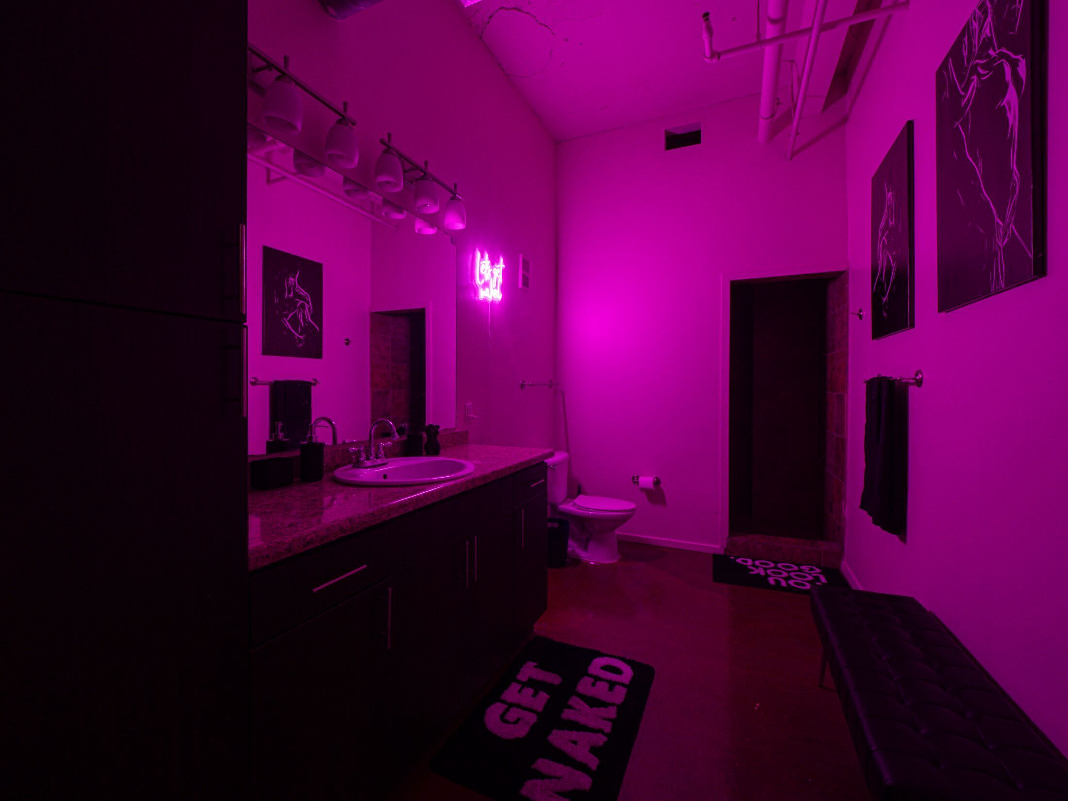 A bathroom with a pink hue, a sink, a toilet, and a mirror.