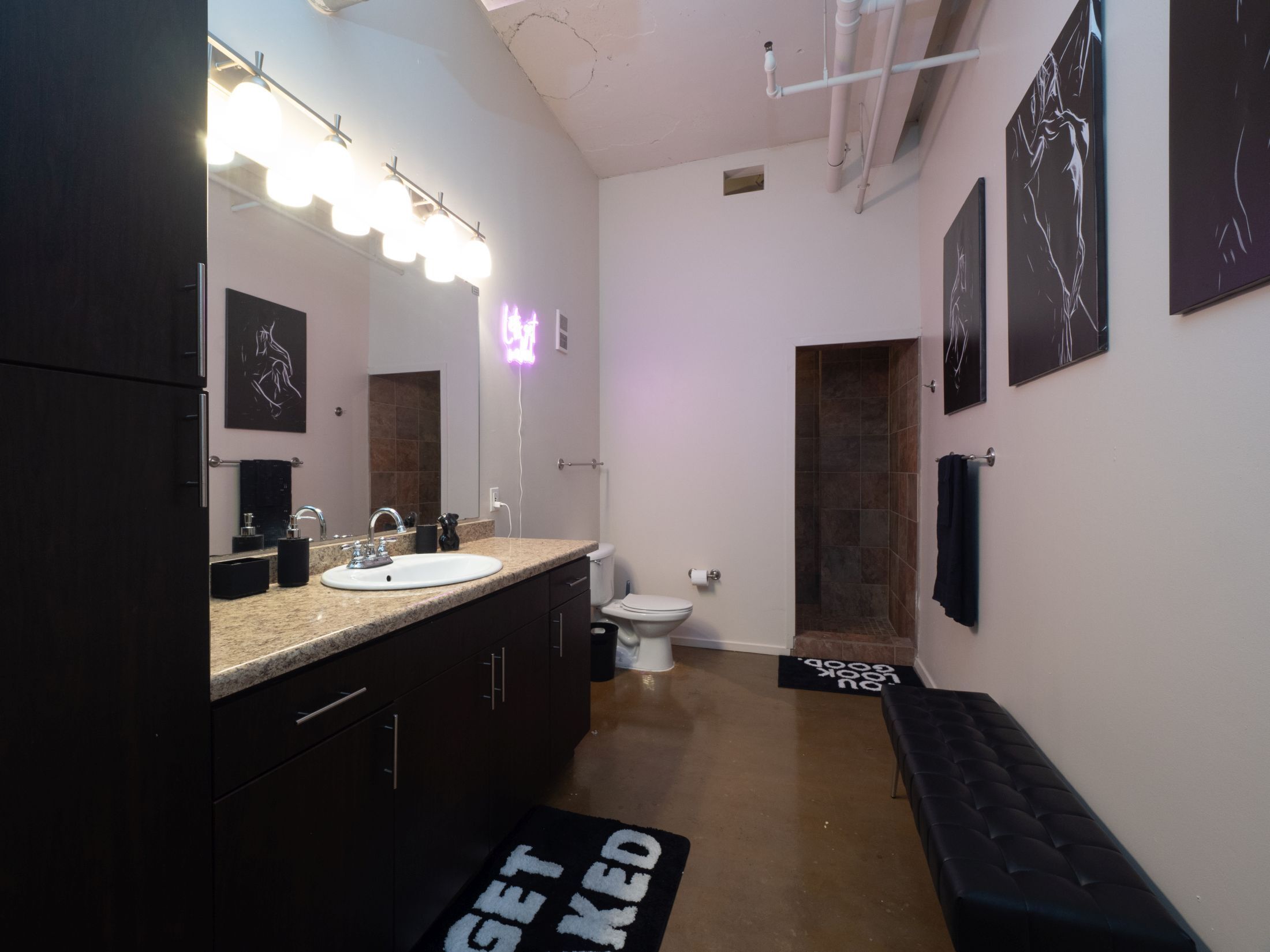 Une salle de bain moderne avec un grand miroir, un meuble-lavabo, un lavabo et des toilettes. On y trouve des serviettes noires et un banc noir.
