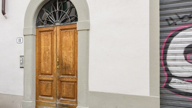 A double wooden door with a small window above it, set in a white building with a metal shutter on the right. - Tripoli apartment in Florence by Mmega (Firenze)