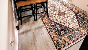 Un comedor con una mesa de madera y un banco, una alfombra estampada, un microondas y una ventana con vistas a árboles.