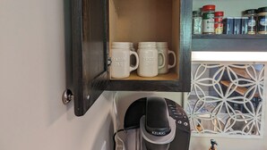 Una cafetera sobre una encimera, con una jarra de café, una taza y una botella de jabón para manos.