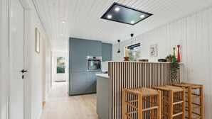 A modern kitchen with a central island, wooden bar stools, and a large window overlooking a garden.