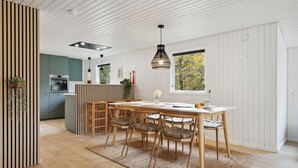 A modern kitchen with a central island, wooden dining table with chairs, and a large window with a view of trees.