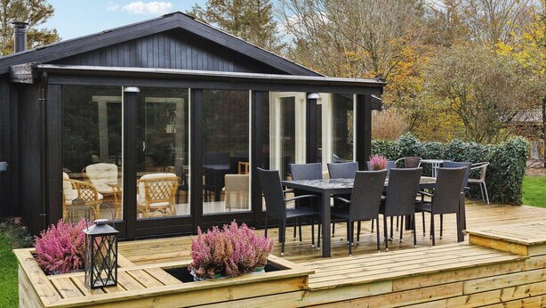 A conservatory with a wooden deck, seating area, and potted plants.