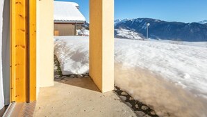 A snowy mountain landscape with a clear sky, a building with a snow-covered roof, and a stone pathway leading to an entrance.