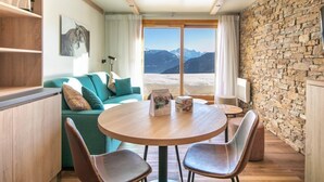 A cozy living area with a round wooden table, two leather chairs, a teal sofa, and a stone wall.